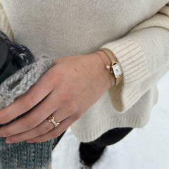 A woman wearing the Quadro Mini & Pavé Crystal Gold Set, featuring a gold rectangular watch with a white dial and a matching pavé crystal bracelet, styled with a cream knit jumper and gold ring in a winter setting.