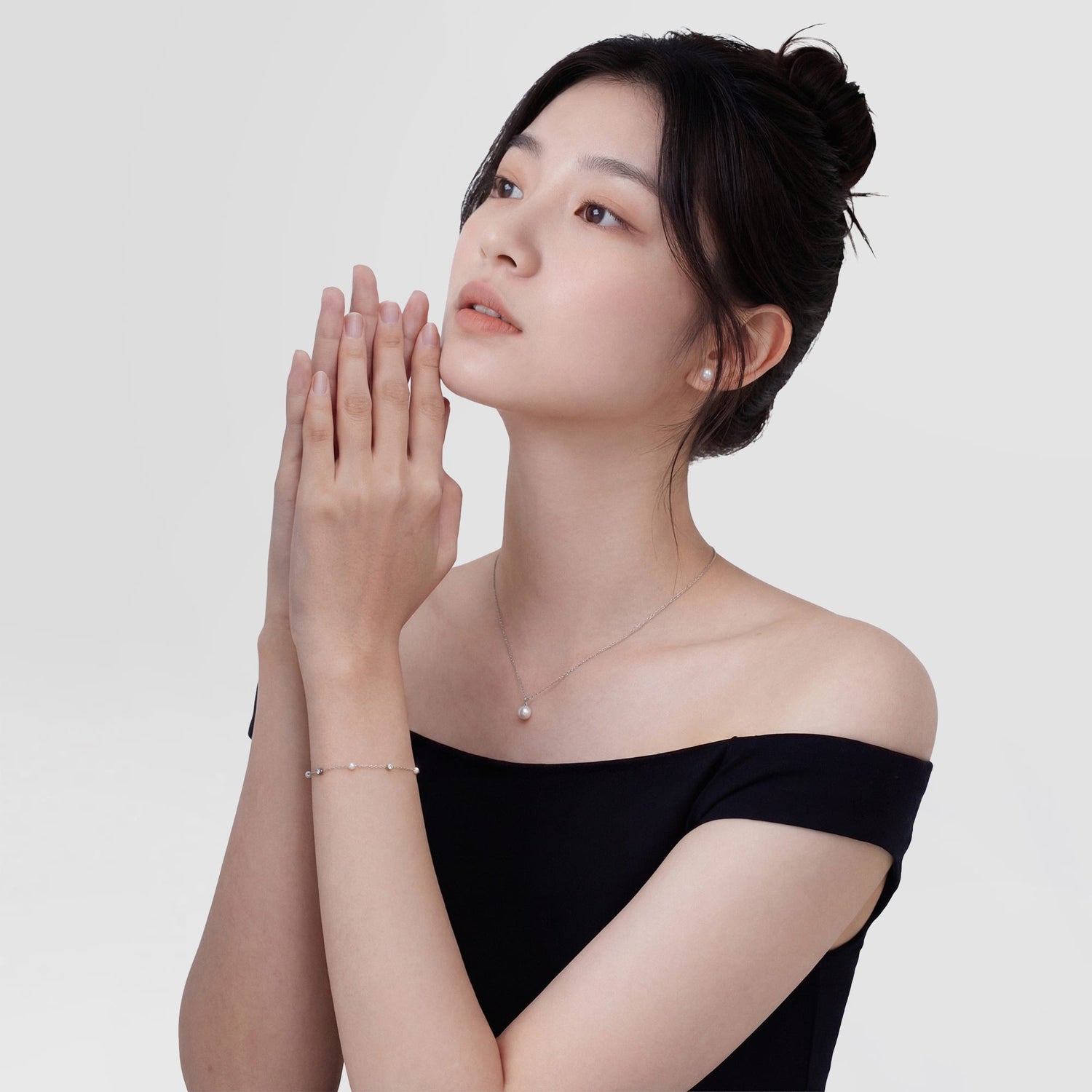 A woman wearing the Pearl Bracelet Silver on her wrist, showing its delicate silver chain with alternating pearls and cubic zirconia, styled with a matching pearl necklace and an off-shoulder black dress for an elegant, minimalist look.