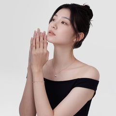 A woman wearing the Pearl Bracelet Silver on her wrist, showing its delicate silver chain with alternating pearls and cubic zirconia, styled with a matching pearl necklace and an off-shoulder black dress for an elegant, minimalist look.