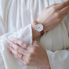A woman wearing the Petite Durham Rose Gold watch with a light brown leather strap and minimalist white dial, styled with a white blouse for an elegant, everyday look.