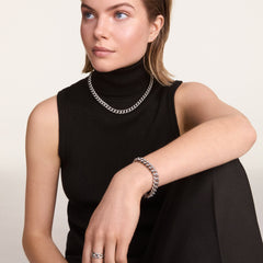 A woman wears the Chunky Chain Necklace Silver with matching bracelet and ring, styled over a black sleeveless polo neck top for a modern, sophisticated look.