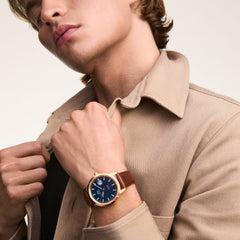 A man wearing the Iconic St Mawes Automatic Rose Gold watch with a blue enamel dial and brown Italian leather strap, styled with a beige jacket for a smart-casual look.