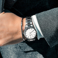 Iconic Link Silver watch by Daniel Wellington worn with a matching silver bracelet, featuring a minimalist eggshell white dial and polished stainless steel strap, styled with a formal suit for a refined business look.