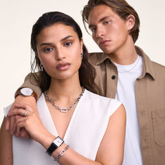 A woman wearing the Crystal Link Necklace Silver styled with a sleeveless white top, showcasing its chunky chain and crystal-embellished link, paired with matching silver accessories and a watch for a modern, elegant look.
