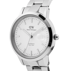 Daniel Wellington Iconic Link Automatic Silver men’s watch with a stainless steel bracelet, minimalist white enamel dial, glow-in-the-dark markers, and a magnified date window, shown from a side angle.