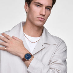 A man wearing the Classic Day Display St Mawes Rose Gold Arctic watch, featuring a blue textured dial, rose gold case, and brown leather strap, styled with a light jacket for a smart, modern look.