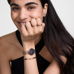 Petite Melrose Black Rose Gold watch worn on a woman's wrist, styled with a matching rose gold bracelet and a sleeveless black top, showcasing its elegant mesh strap and minimalist black dial.