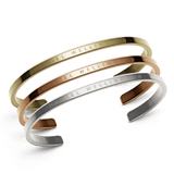 Three minimalist cuff bracelets in rose gold, gold, and silver tones, each engraved with the Daniel Wellington logo, displayed together to highlight their polished stainless steel finish and versatile styling.