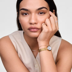 A woman wearing the Juliette Braided Mesh White Sunray Gold watch, featuring a gold braided mesh strap and oval white sunray dial, styled with neutral clothing and delicate jewellery for a modern, understated look.