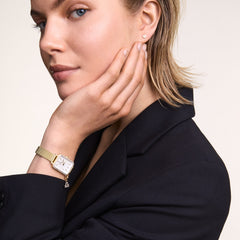 Woman wearing the Quadro Crystal Zodiac Evergold Set gold ladies watch with a rectangular crystal-set bezel, white mother of pearl dial, gold mesh strap, and removable zodiac charm, styled with a black blazer for a sophisticated look.