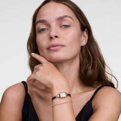 Woman wearing the Classic Tennis Bracelet Apricot Rose Gold, styled with a rose gold watch and a black strappy top, showcasing the slim bracelet’s apricot-coloured crystals and delicate fit for everyday elegance.