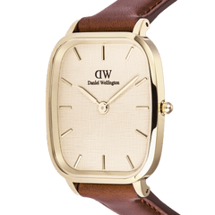 Close-up of the Daniel Wellington Marlon St Mawes Linen Gold men’s watch, featuring a cushion-shaped gold case, linen-textured dial, minimalist gold-tone hour markers, and a brown leather strap.