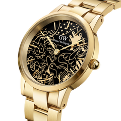 Daniel Wellington Iconic Link Dual Tone Gold watch with a polished gold bracelet and a black dial featuring Steven Harrington’s signature gold illustrations, shown in a close-up angle highlighting its artistic details and premium finish.