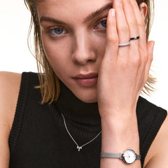 A woman wearing the Crystal Zodiac Chain Necklace Silver with an Aquarius zodiac pendant set with crystals, styled with a black sleeveless top, silver watch, and silver rings for a modern, minimalist look.
