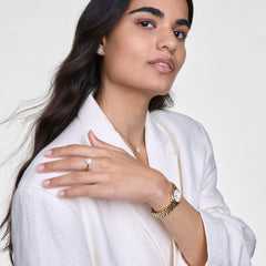 A woman wearing the Audrey Earrings Mother of Pearl Gold, styled with matching gold jewellery and a cream blazer, showcases the elegant stud earrings with mother of pearl centres and sparkling cubic zirconia halos for a refined, coordinated look.