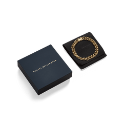 Chunky Chain Bracelet Gold displayed on a black cushion next to a sleek Daniel Wellington gift box, highlighting its polished gold links and elegant presentation for gifting.