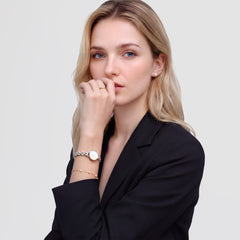 A woman wearing a black blazer styles the Petite Mini Arch 3-Link Two Tone Gold watch on her wrist, showing its slim gold and silver bracelet and petite white dial paired with a delicate bracelet for a polished, everyday look.