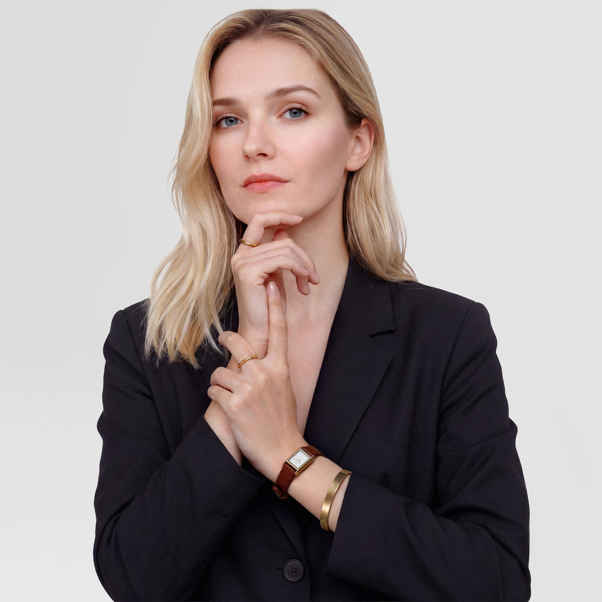 A woman wearing the Bound Mini Light Brown Lizard Gold watch styled with a black blazer, showing the petite gold rectangular case and light brown lizard-embossed leather strap paired with gold jewellery for a polished, modern look.