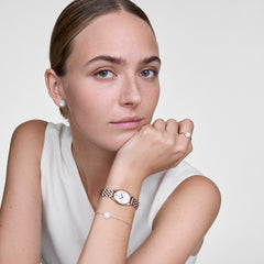 Ophelia Mini Rose Gold ladies watch styled on the wrist with matching jewellery, showing its oval rose gold case, white sunray dial, and slim five-link bracelet paired with a sleeveless white top.