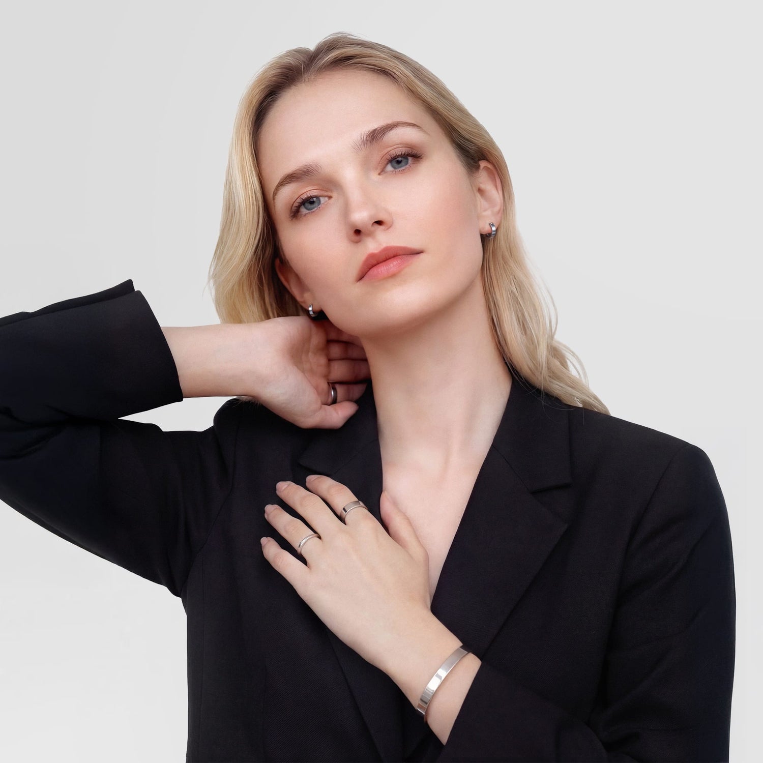 A person wearing the Line Earring Polished Silver 3.5mm, styled with matching silver rings and a bracelet, showcasing the minimalist hoop earring as part of a modern, professional outfit.