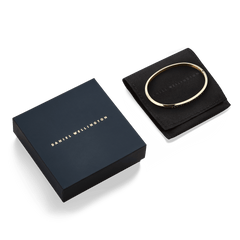 Classic Bangle Gold is presented on a black pouch next to a navy Daniel Wellington gift box, highlighting its polished gold finish and elegant packaging suitable for gifting.