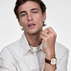A man wearing the Classic Day Display St Mawes Rose Gold Champagne watch, featuring a champagne dial with day and date display, rose gold case, and brown leather strap, styled with a light jacket for a smart casual look.