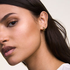 The Daniel Wellington 5-Link Earrings Gold are shown worn on the ear, highlighting their geometric open link design and polished gold finish, styled with dark hair and a white top for a modern, elegant look.