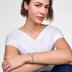 Woman wearing the Mirelle Heart Bracelet Silver with a slim chain and open heart charm set with cubic zirconia stones, styled alongside a silver watch and other jewellery for a polished, everyday look.
