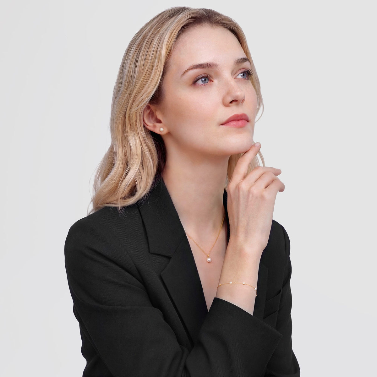 A woman wearing the Pearl Bracelet Gold, featuring alternating white Swarovski glass pearls and cubic zirconia stones on a slim gold chain, styled with a black blazer for a sophisticated, modern look.