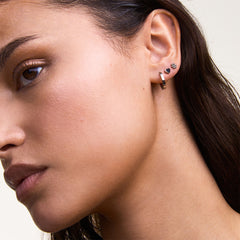 A woman wears the Daniel Wellington Hoop + Heart + Flower Stud Silver Set, showing a polished silver hoop, a heart-shaped stud, and a delicate flower stud styled together on one ear for a modern, layered look.