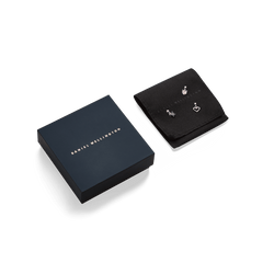 Daniel Wellington gift box alongside a black jewellery pouch, showcasing three silver charms including a heart, a crystal, and a crescent shape.