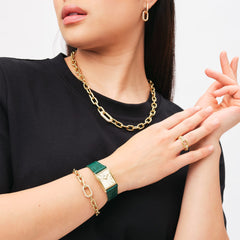 A woman wearing the Bound Crocodile Champagne Sunray Gold watch with a green crocodile-pattern leather strap, styled with gold jewellery including a chain necklace, bracelet, and ring, creating a chic and coordinated look.