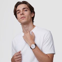 A man wearing the Classic Roman Numerals Date Dark Brown Croc Belly Gold watch, featuring a gold case, white dial with Roman numerals, and a dark brown crocodile-embossed leather strap, styled casually with a plain white T-shirt.
