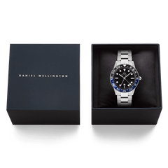 Daniel Wellington Iconic GMT Link Black Blue Ceramic Bezel Silver watch presented in its branded gift box, featuring a black dial, blue and black ceramic bezel, and a silver stainless steel bracelet.